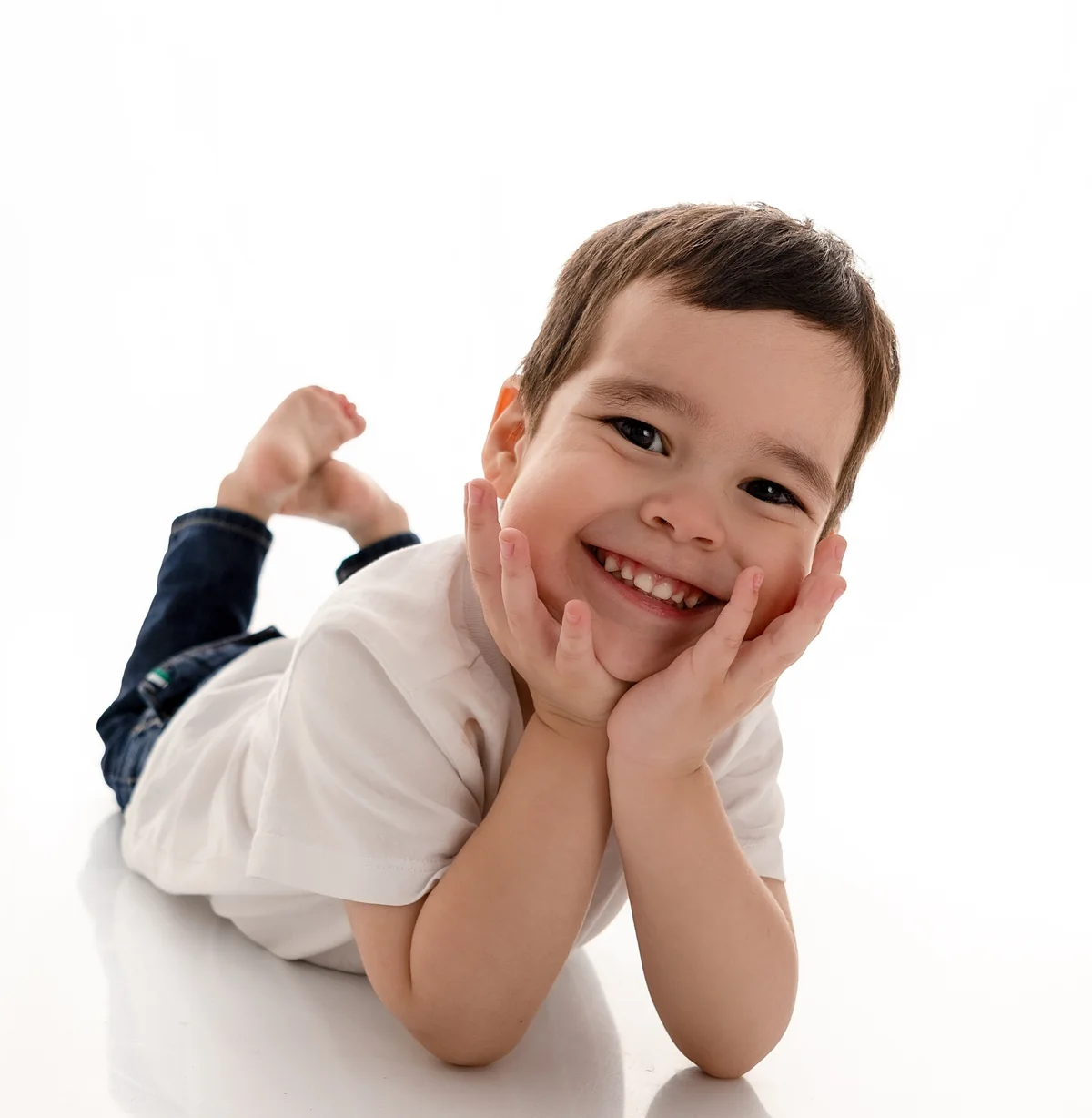 Niño sonriente acostado en el piso con las manos en la cara